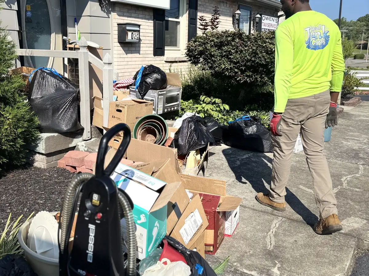 Local Junk Guys crew member clearing a curbside pile of boxes, bags and household junk outside a Nashville property